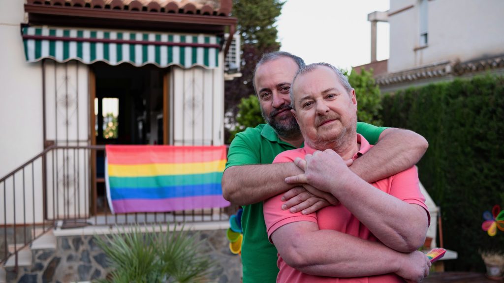 Older Gay Couple Hugging Outside Home